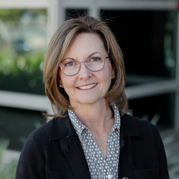 Kim McCrady, smiling, wearing glasses and a dark cardigan.